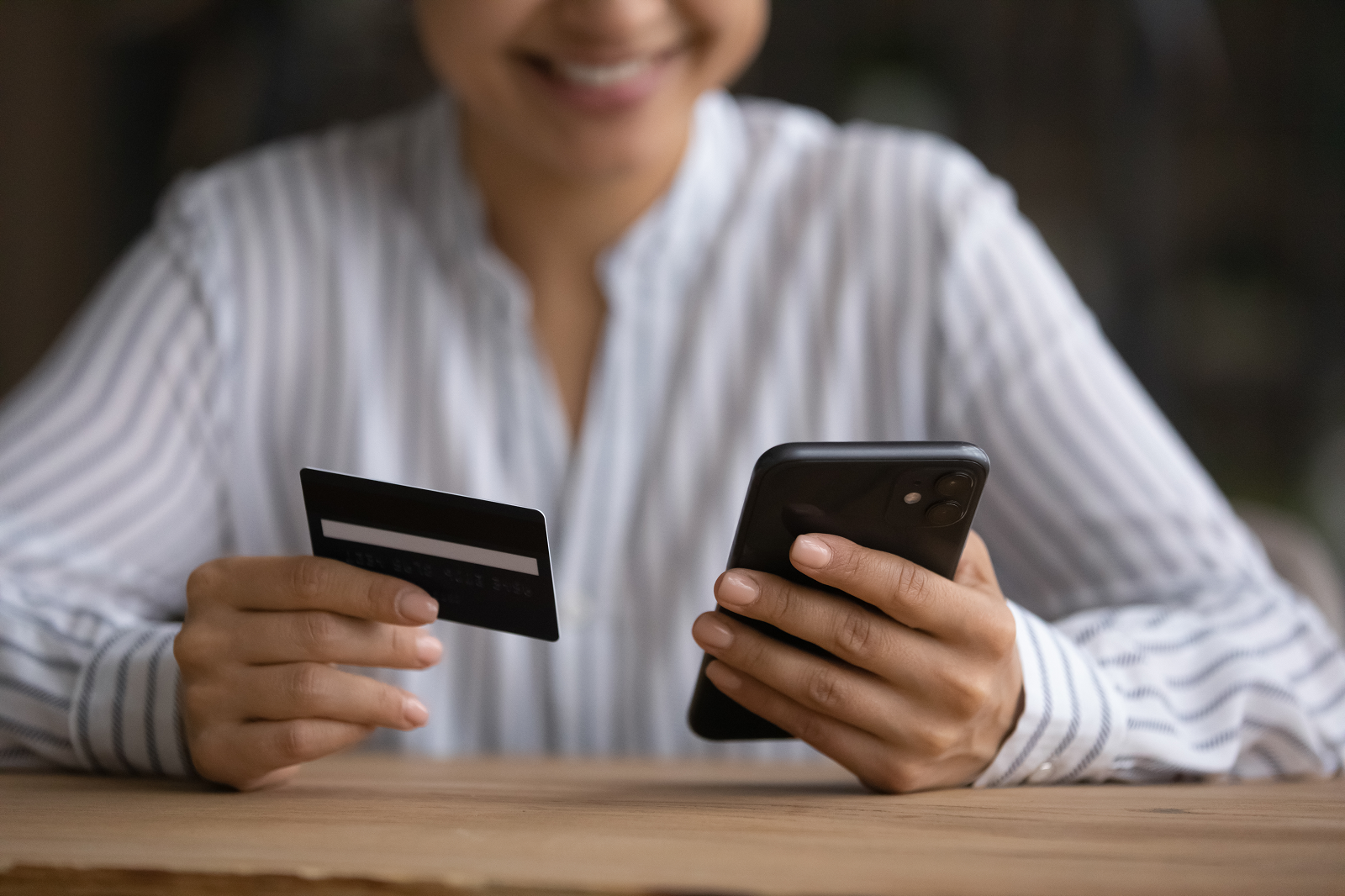 Mulher sorridente segura o celular em uma mão e um cartão de crédito na outra para realizar um pagamento pelo WhatsApp